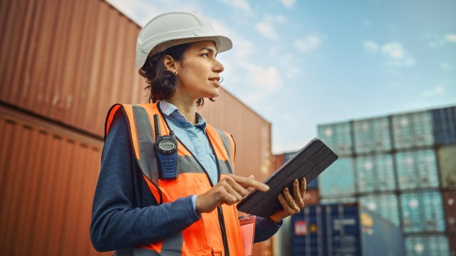 Supply chain manager using a tablet at a container shipping port during ongoing tariff developments