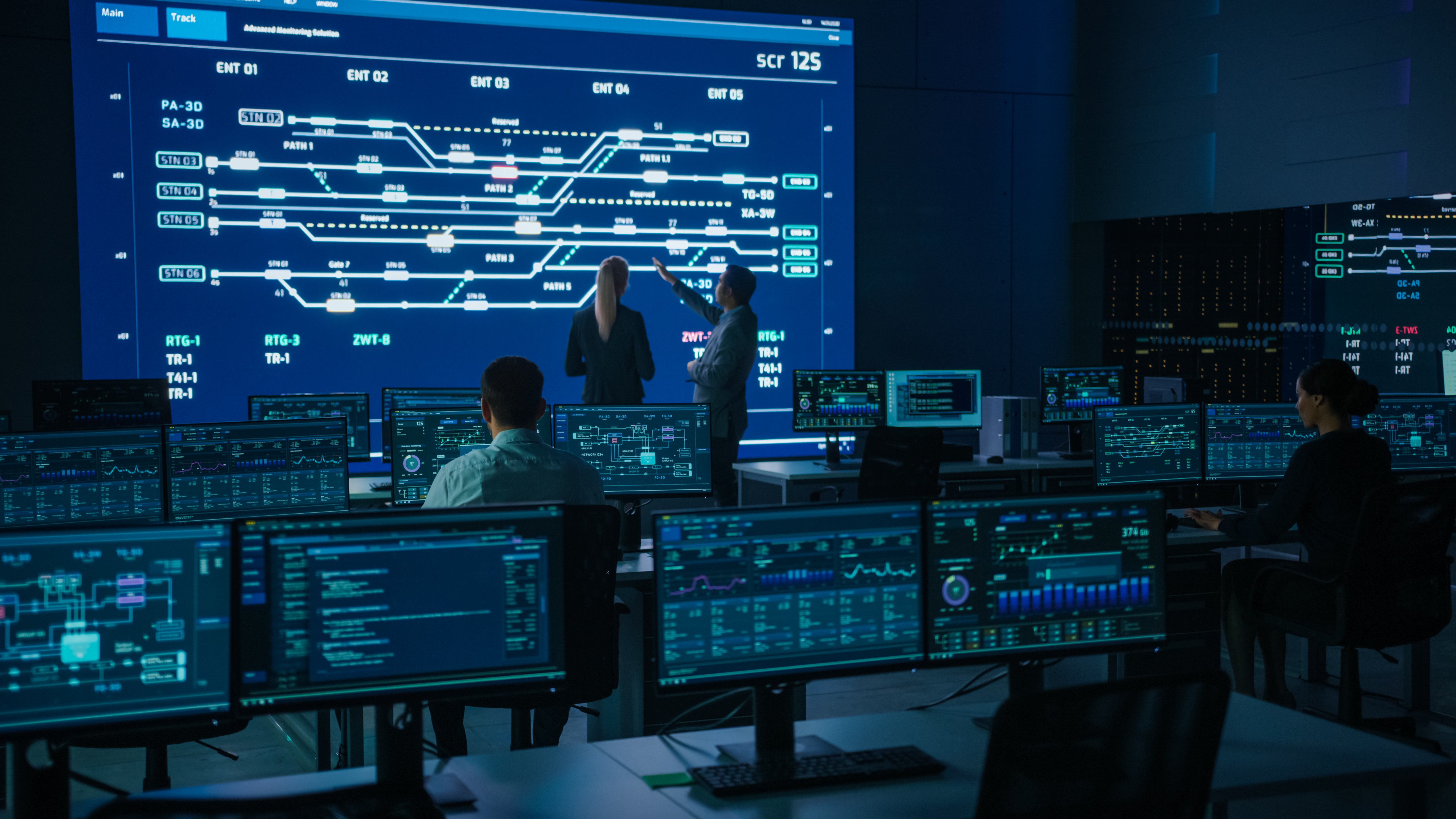 Network operations team monitoring telecom infrastructure on a multi-screen control room display