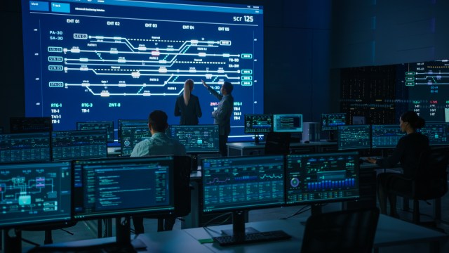 Network operations team monitoring telecom infrastructure on a multi-screen control room display