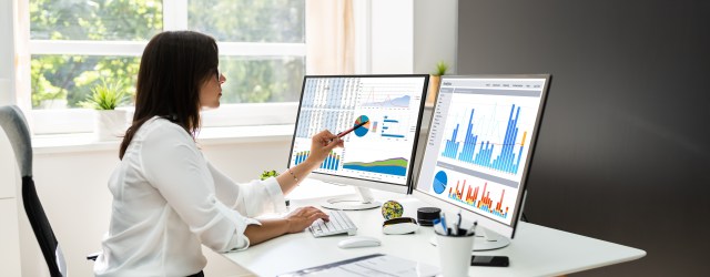 Analyst reviewing AI performance data and KPI dashboards across dual monitors