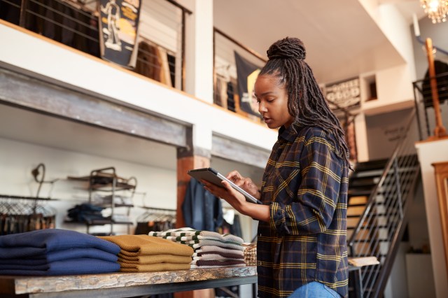 Small business owner using a digital tablet to check clothing inventory in a retail store