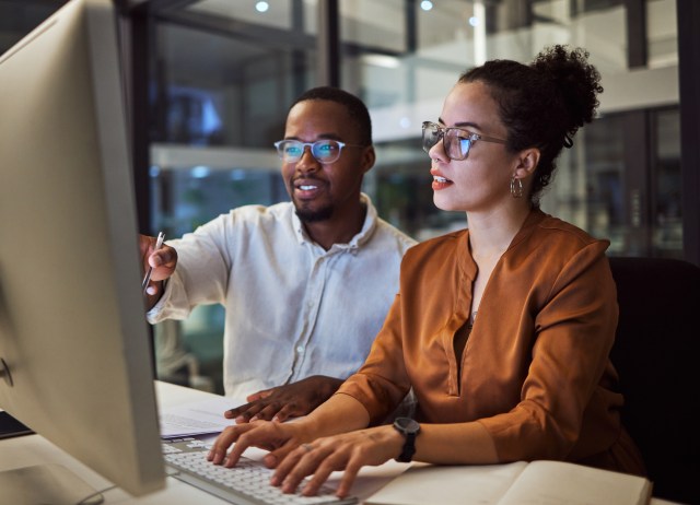 Two enterprise employees collaborating on AI training at a computer workstation, representing hands-on foundational AI literacy in the workplace.