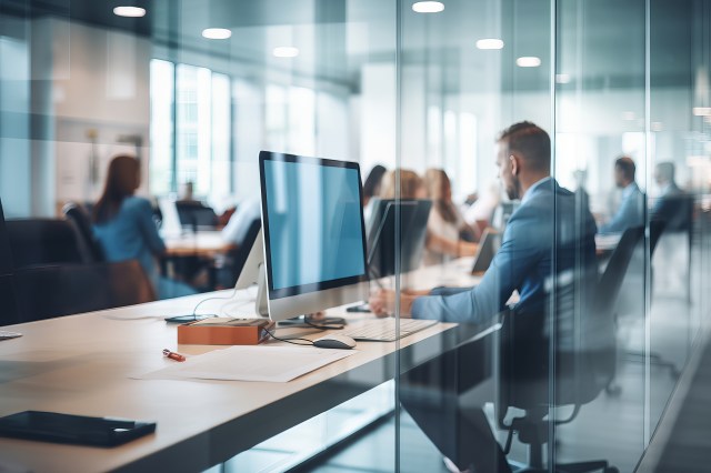 Professionals working at desks in a modern glass-walled office environment.