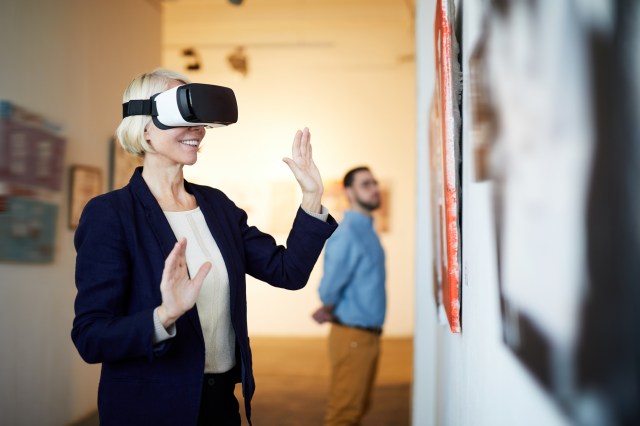 Woman wearing a VR headset interacts with an exhibit at an art gallery, illustrating consumer adoption of extended reality technology