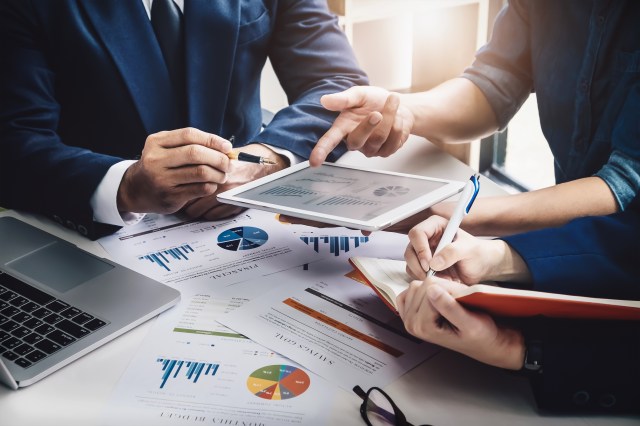 Business consultants reviewing financial and budget charts on a tablet and printed reports during a contract analysis meeting