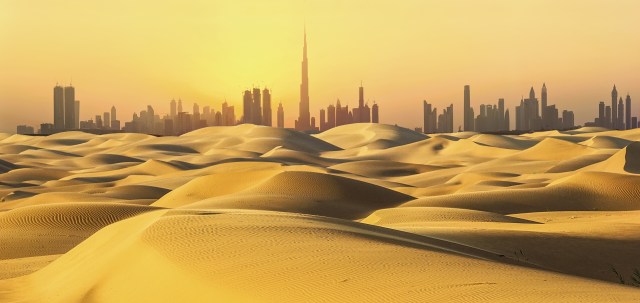 Dubai skyline with Burj Khalifa silhouetted against desert dunes at sunset