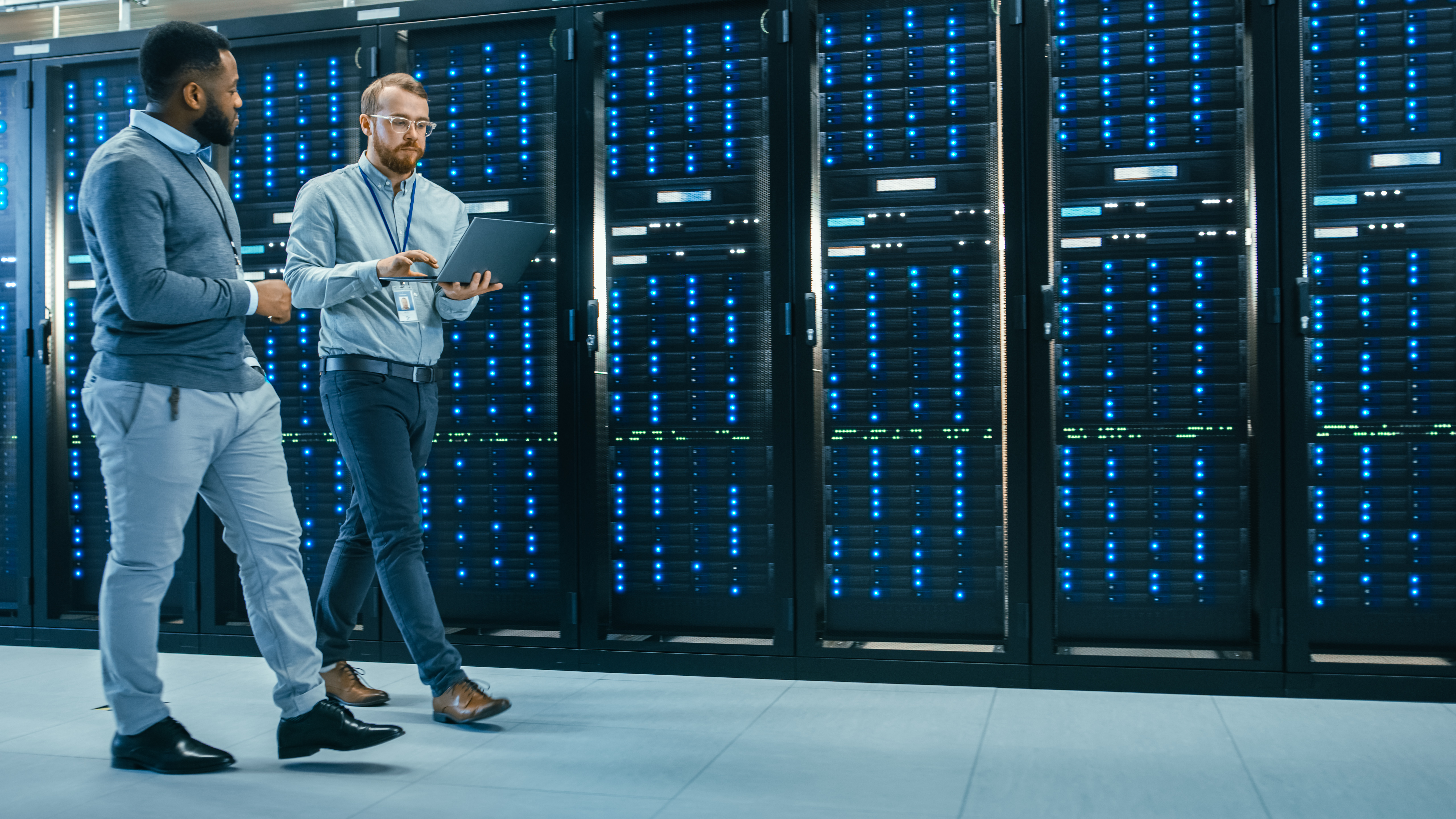 IT technician and engineer reviewing diagnostics on a laptop while walking past server racks in a data center