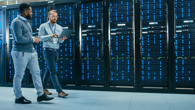 IT technician and engineer reviewing diagnostics on a laptop while walking past server racks in a data center