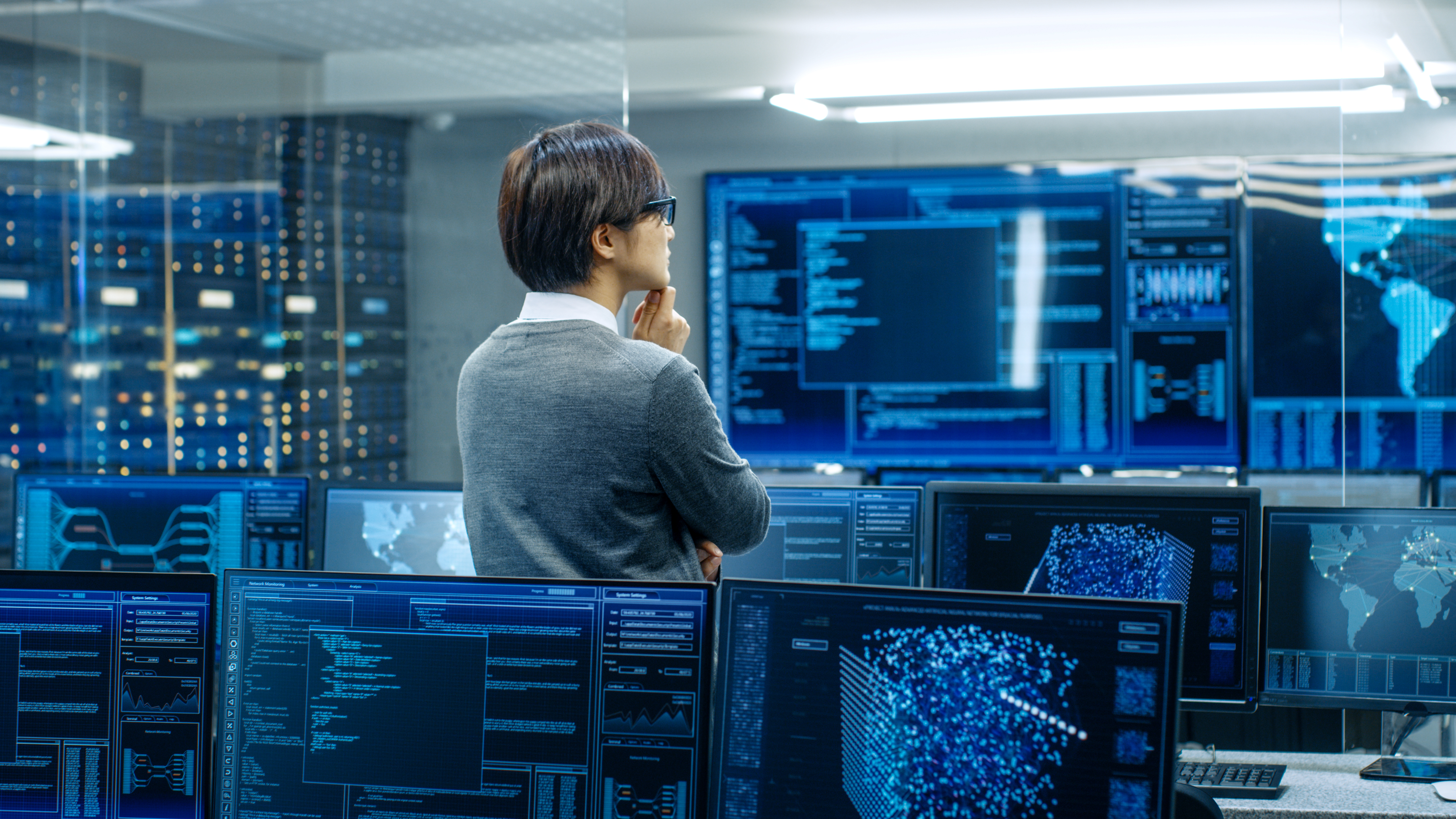 IT security operator in a control room monitoring multiple screens displaying network data, system analytics, and world map visualizations