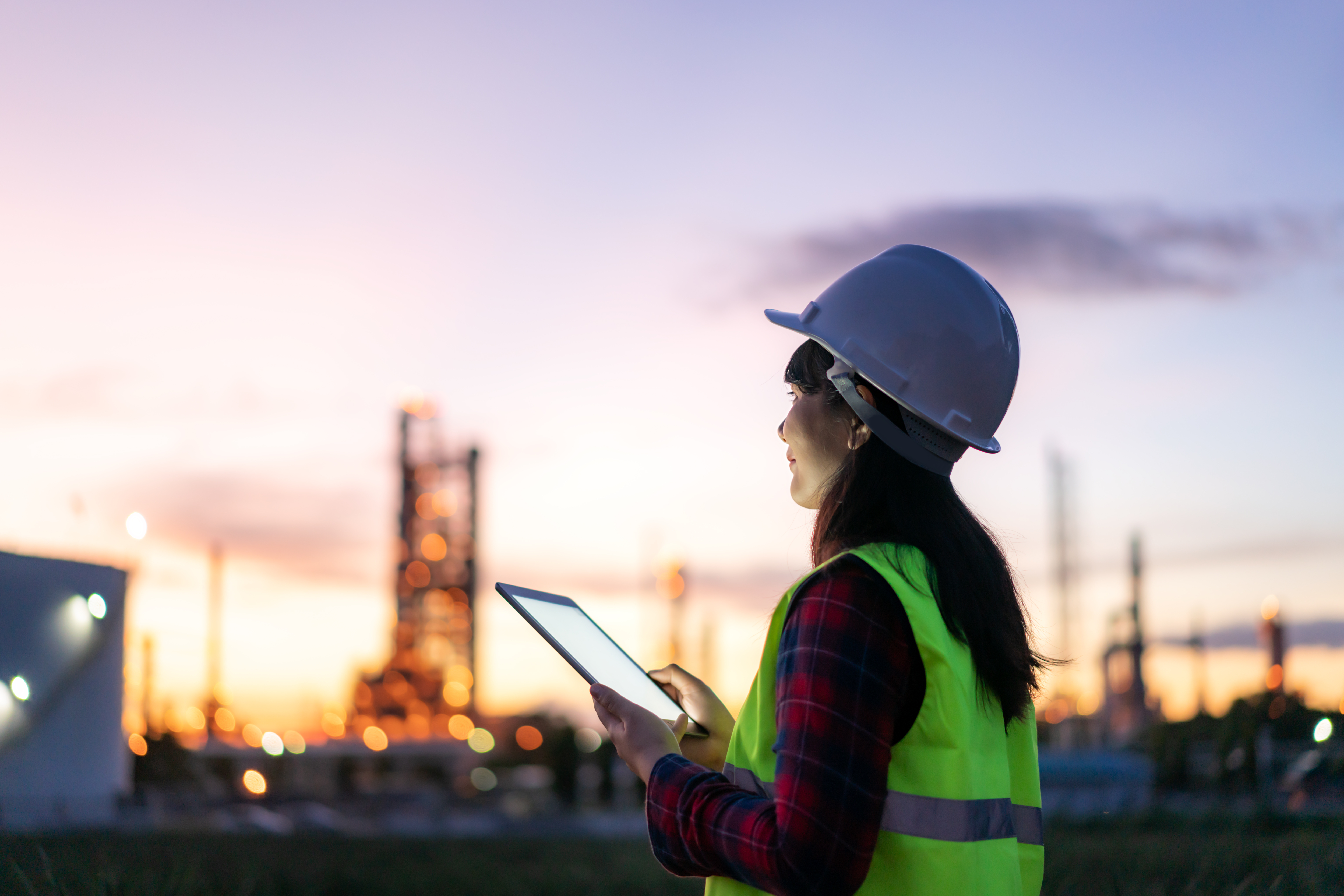 Engineer in hard hat and safety vest reviewing plant data on a tablet
