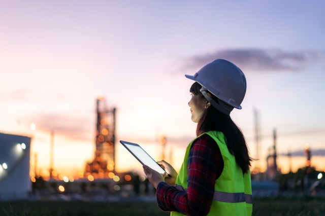 Engineer in hard hat and safety vest reviewing plant data on a tablet